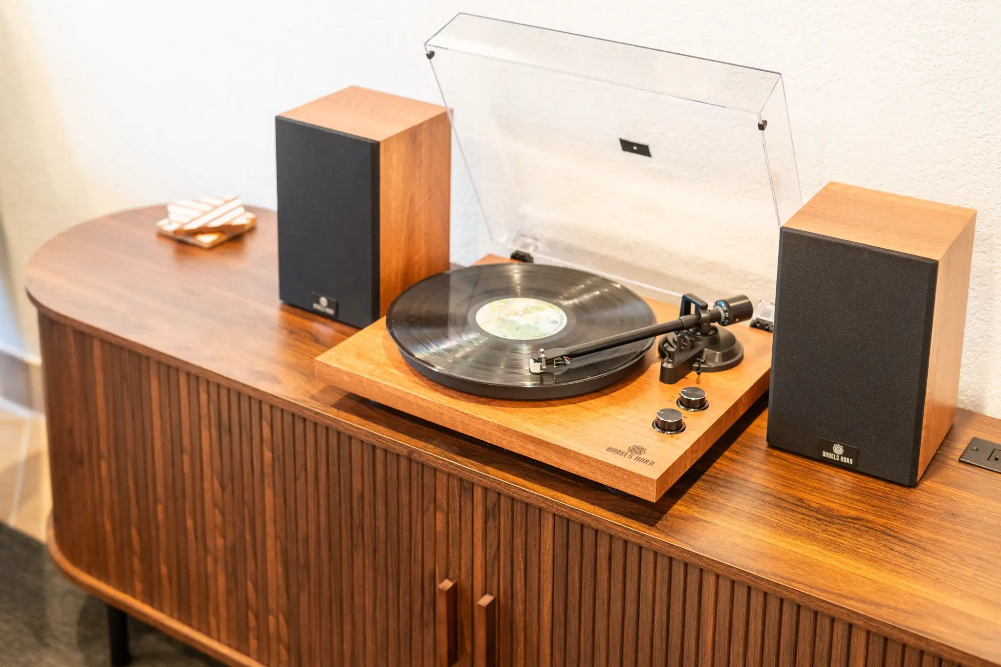 A modern wooden turntable setup with two matching speakers sits on a stylish wooden console cabinet.