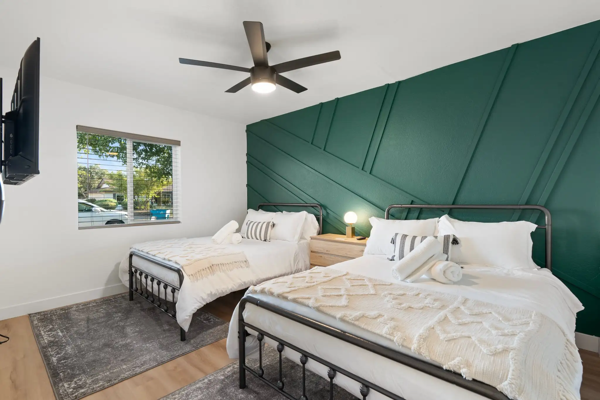 A bright bedroom featuring two beds with white linens and dark metal frames against an emerald green wall with geometric wood paneling.