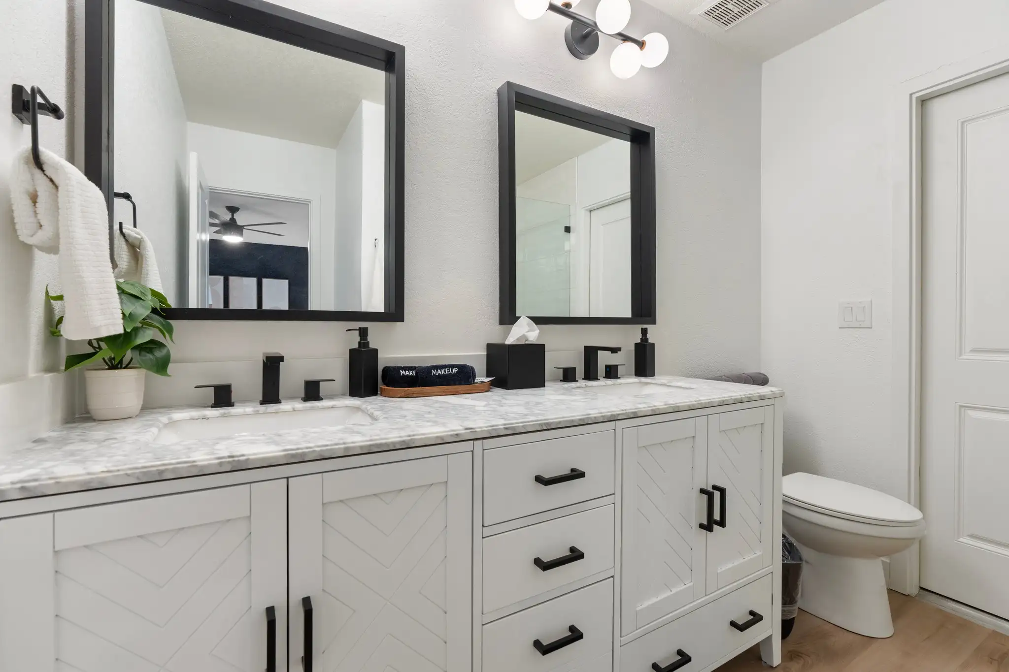 A contemporary double bathroom vanity with white chevron cabinets, a marble countertop, black faucets, and rectangular mirrors, set in a bright white room.