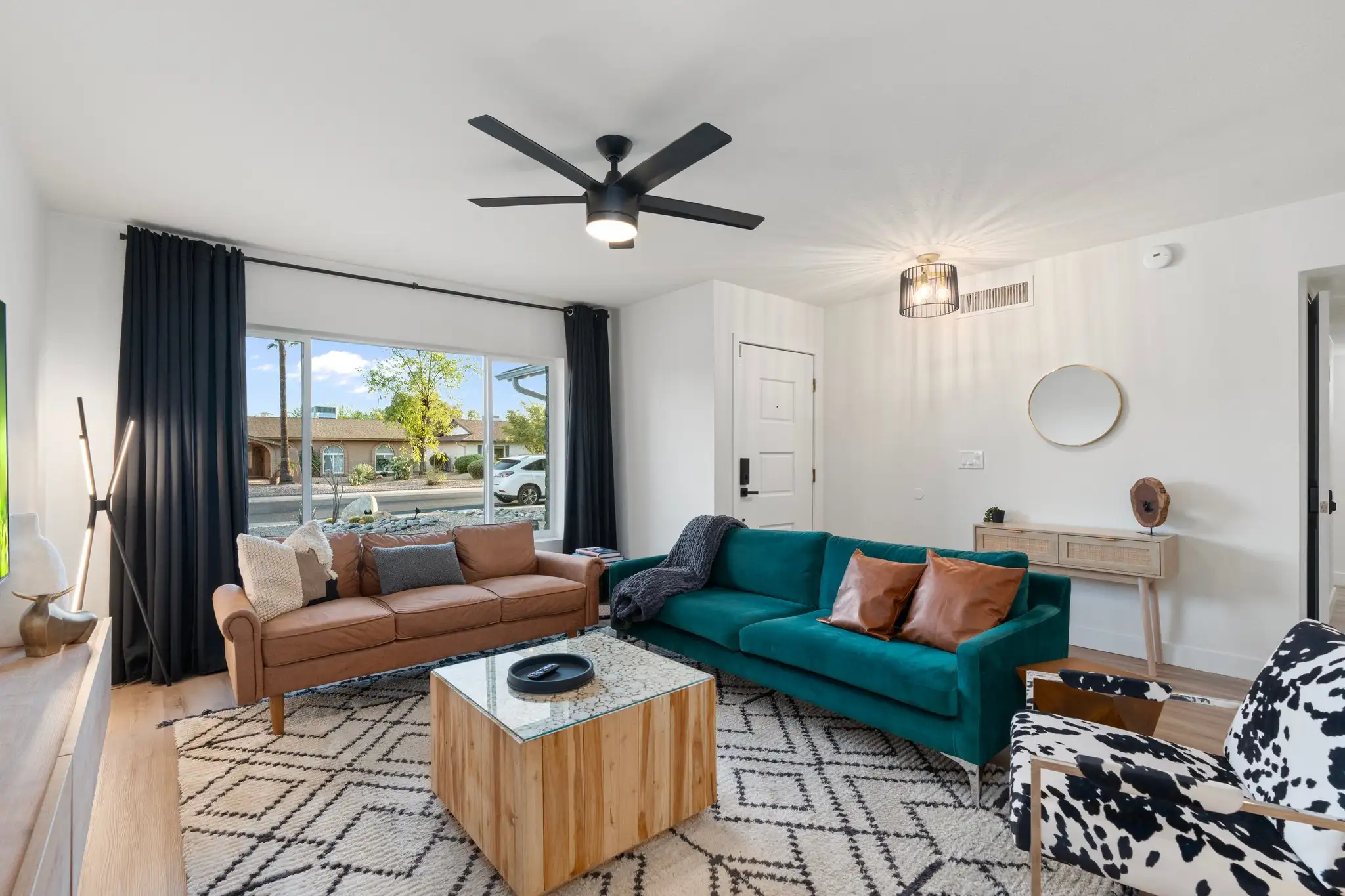 A modern, bright living room features a contrasting brown leather and teal velvet sofa setup over a bold black and white geometric rug.