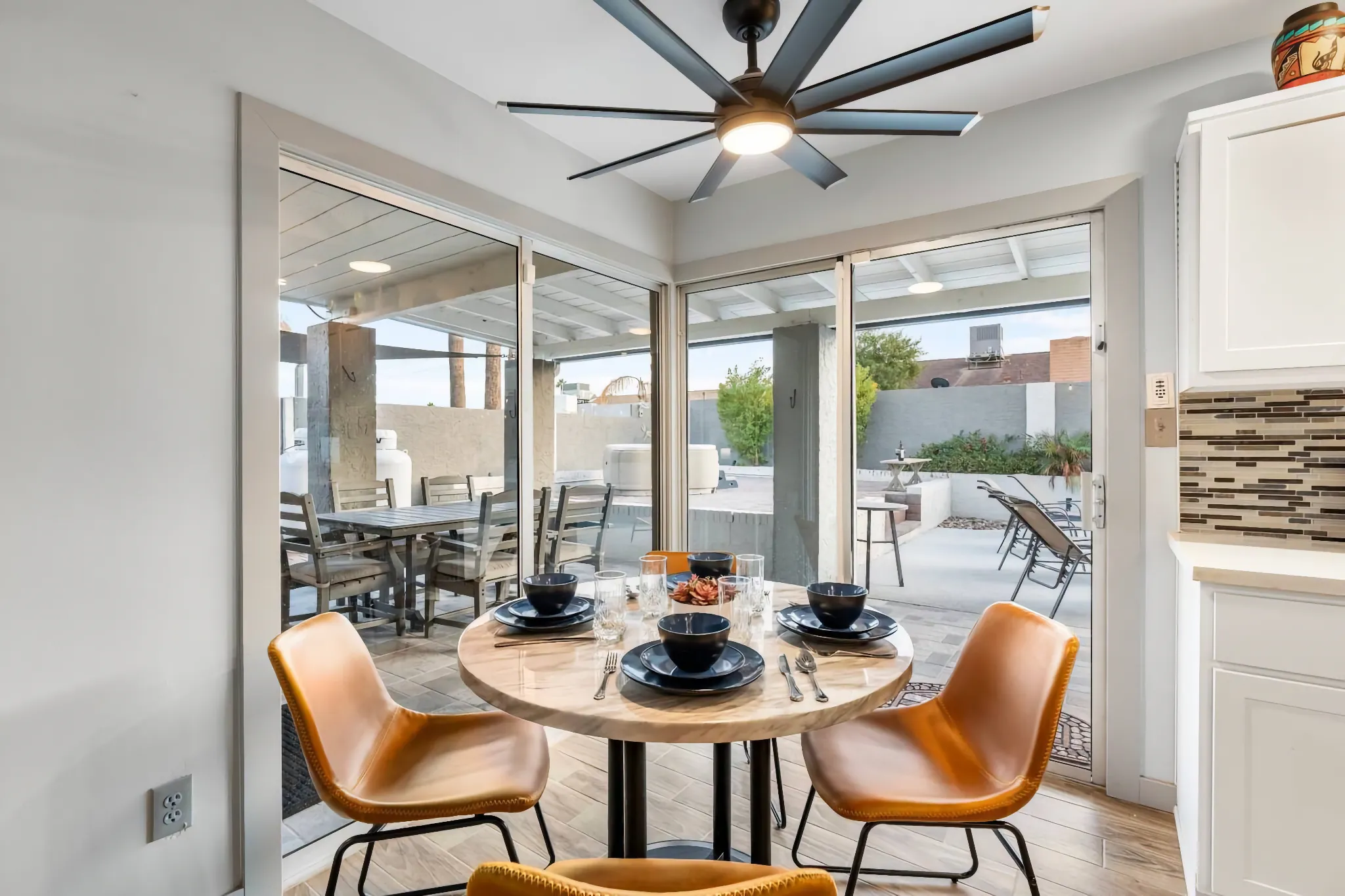 An indoor dining area with a round stone table set for four, featuring large glass doors that open onto a furnished patio with an outdoor dining table.