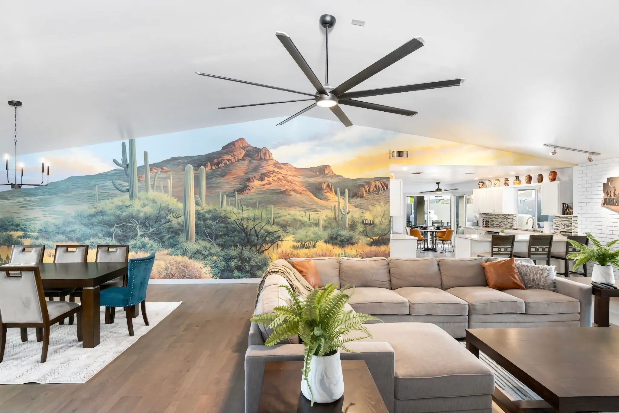 An open-concept living space featuring a stunning wall mural of a desert mountain landscape, a grey sectional sofa, and a modern dining area.