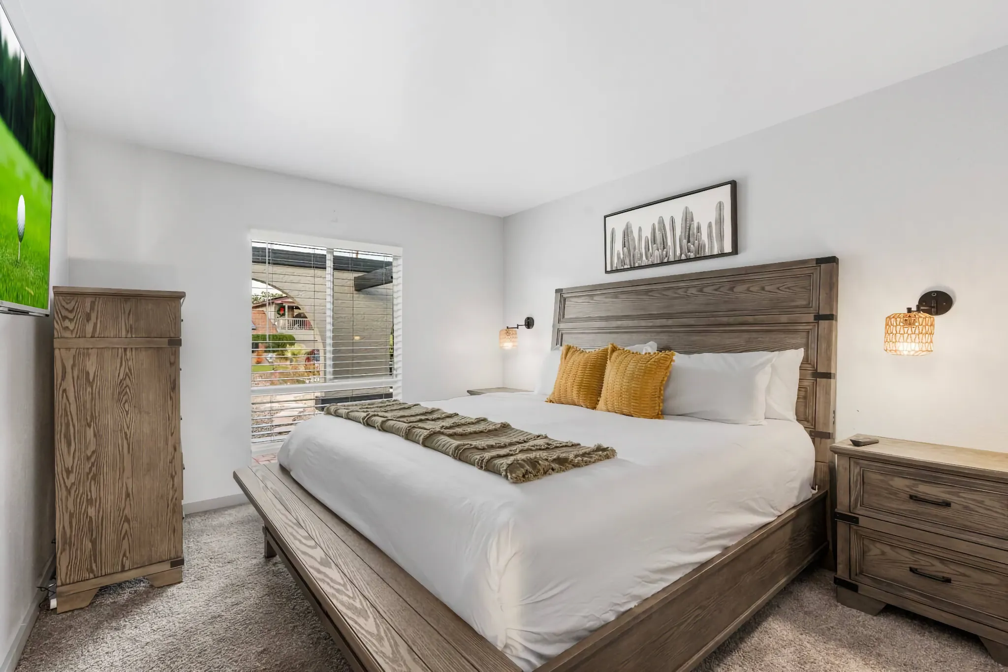 A comfortable vacation rental bedroom with a light gray wood king bed, matching dresser, and two nightstands. The bed has white linens and yellow accent pillows.