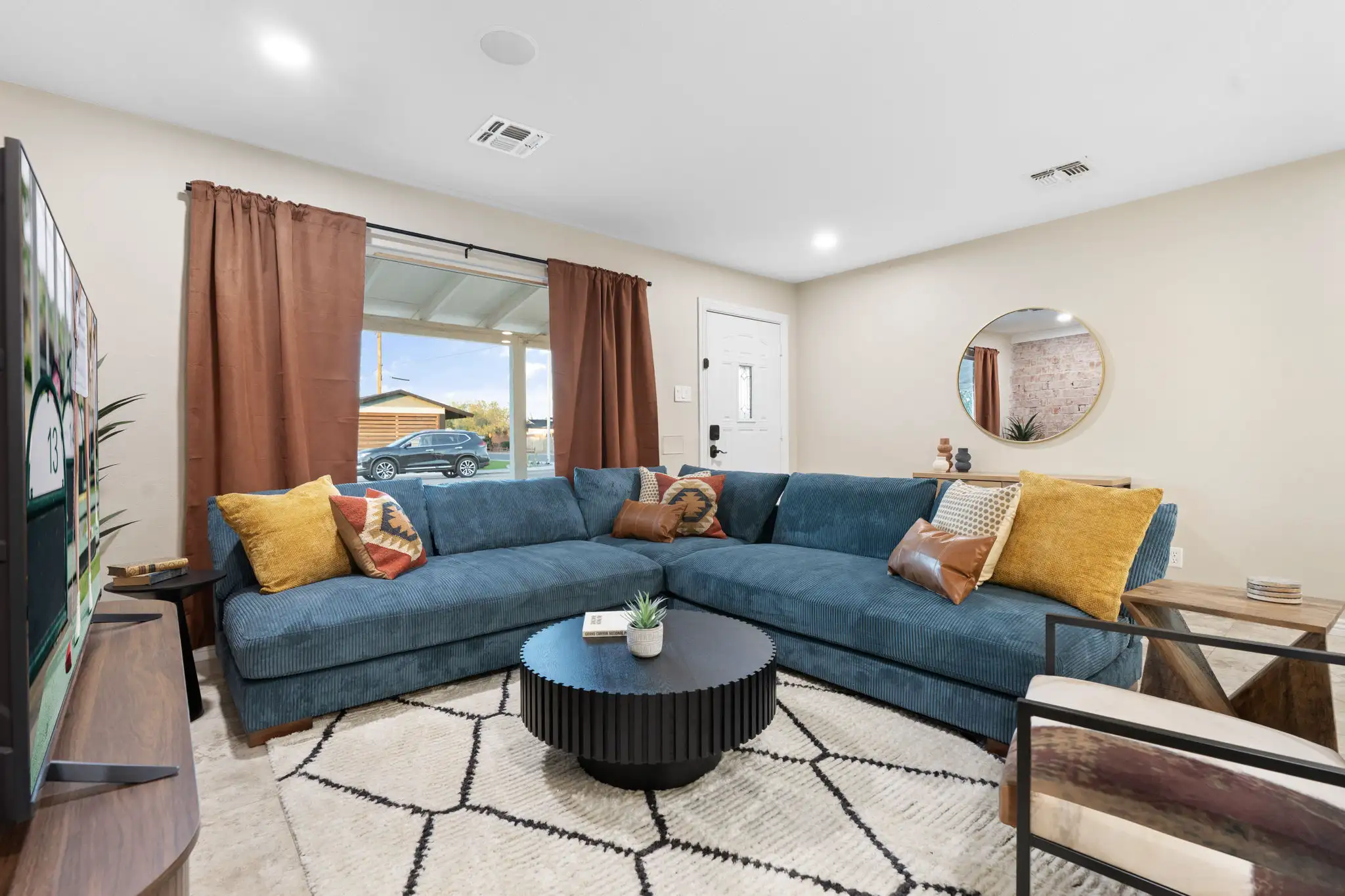 A welcoming, modern living room area with a large blue sectional sofa, assorted throw pillows, and a black fluted coffee table on a white patterned rug.