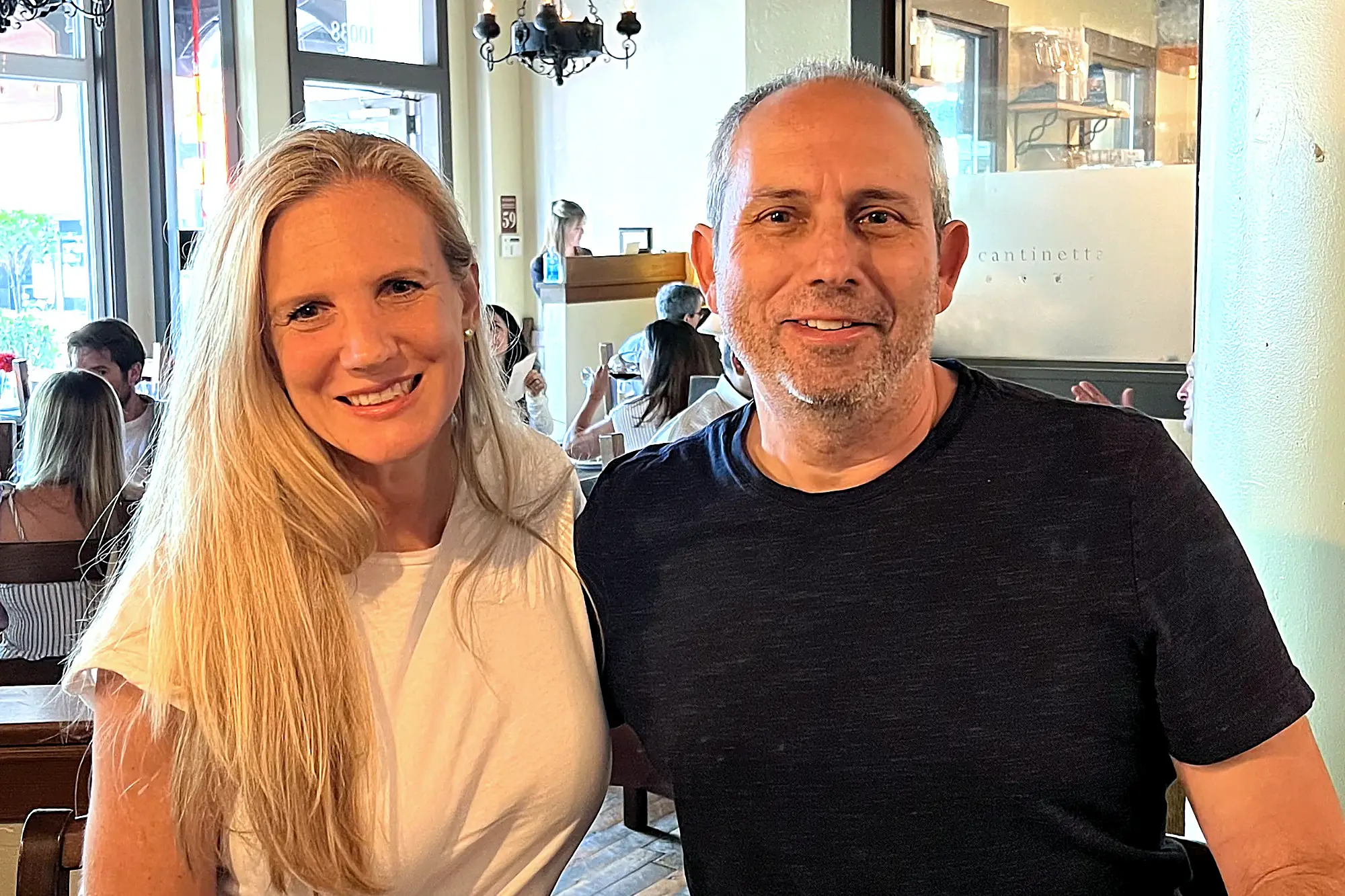 Owners Aharon and Allyson Kessary smile warmly, posing together in a brightly lit restaurant with other patrons visible in the background.